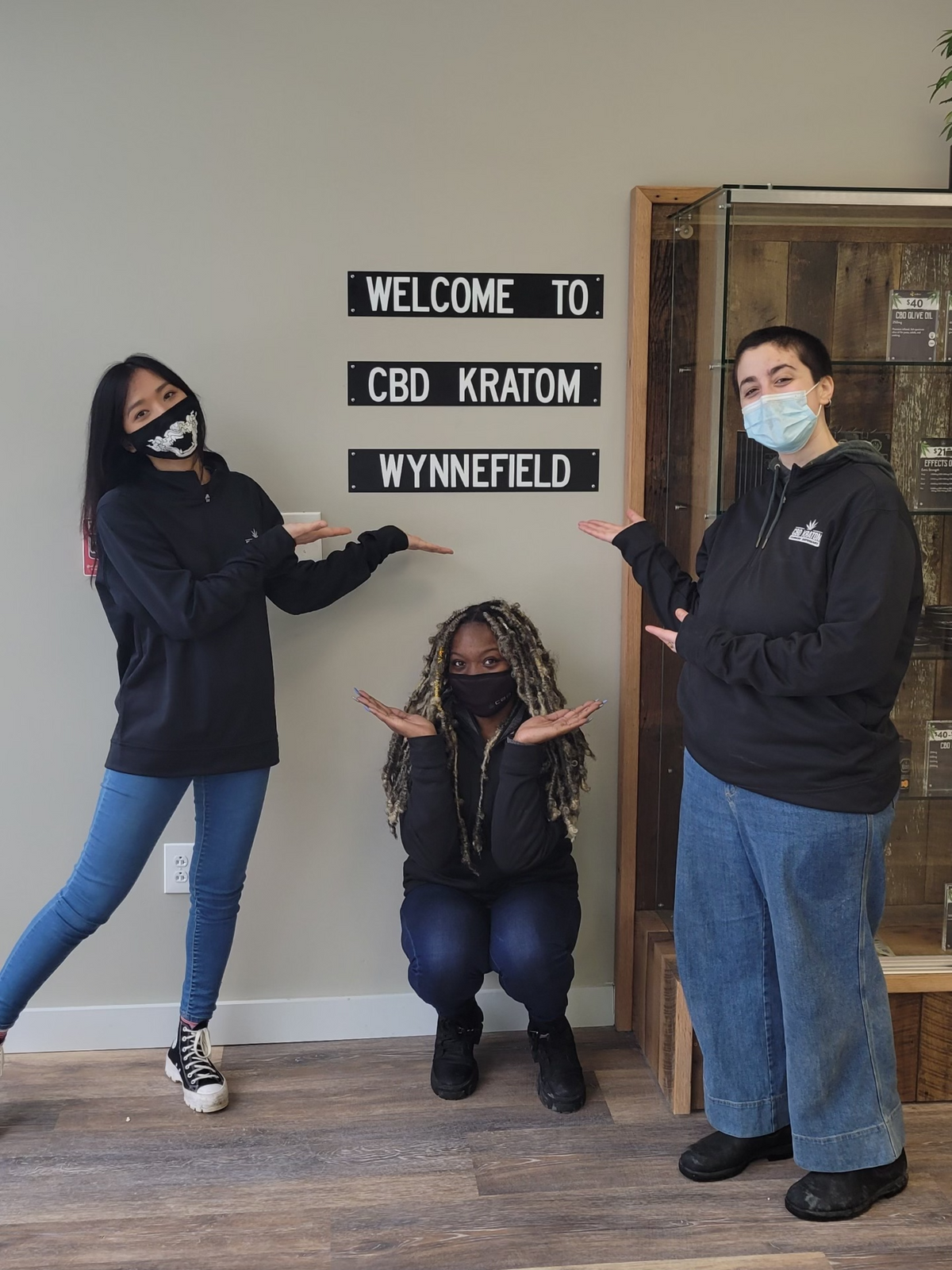 Three CBD Kratom team members in branded hoodies posing beside a Welcome to CBD Kratom Wynnefield sign in Philadelphia.