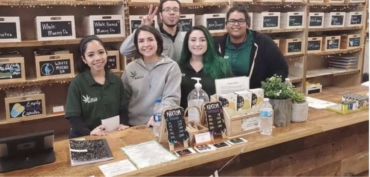Five CBD Kratom team members smiling behind a store counter lined with kratom displays.