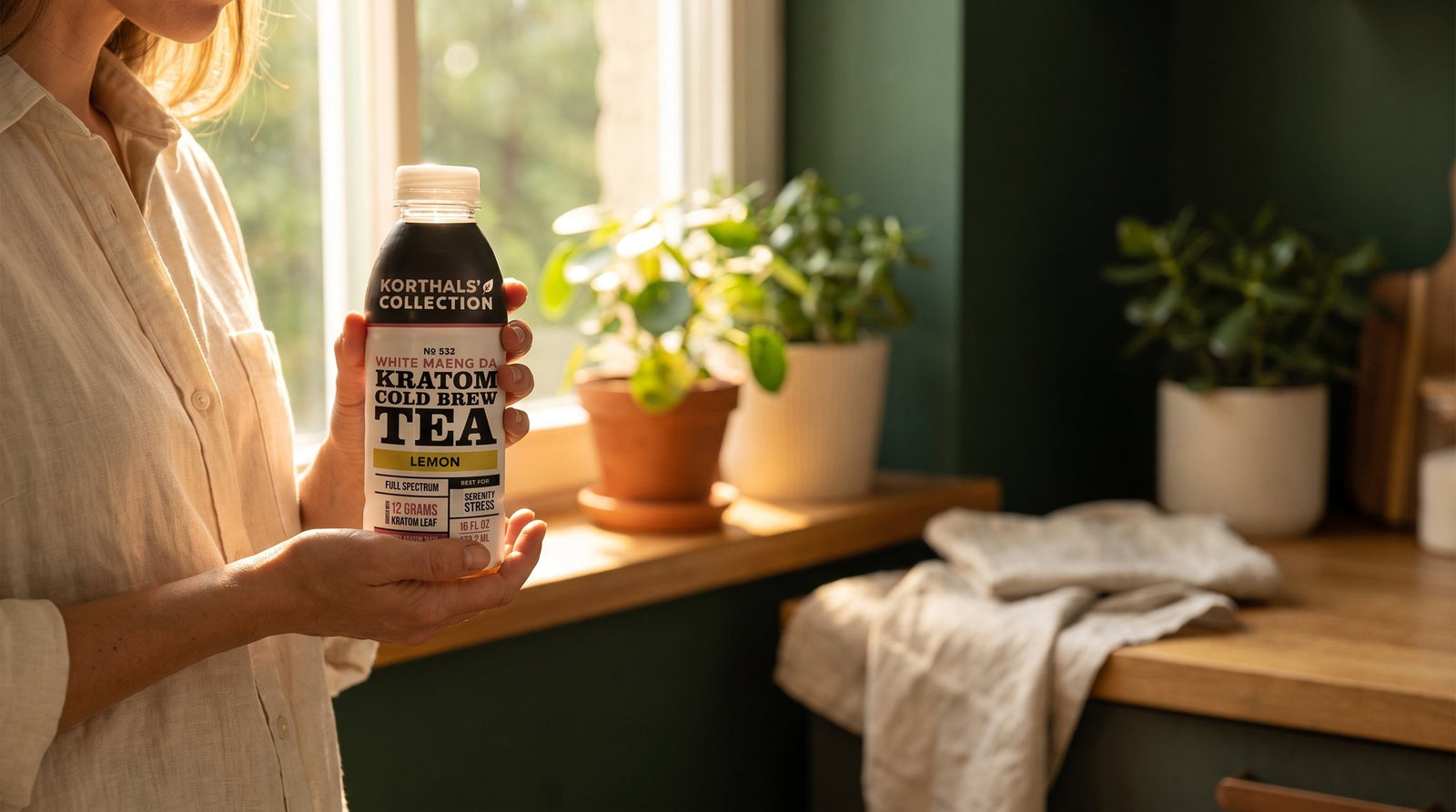 Woman holding Korthals Collection White Maeng Da cold brew tea in a sunlit morning kitchen